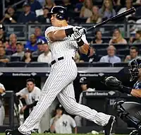 A man wearing a Yankees pinstripe uniform swings at a pitch.