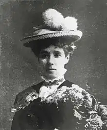 Bust-length, black and white photograph of a woman wearing a hat and a high collar