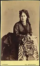 Portrait of a woman in Victorian dress leaning on a support.