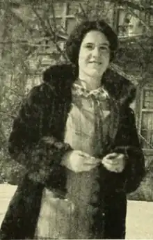A smiling young white woman with dark hair, wearing a fur coat and standing outdoors