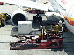 A ULD loader lifting a unit load device (ULD) from apron dollies to an aircraft's cargo bay