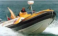 white, black and yellow rigid inflatable boat passing the photographer at high speed, with yellow-coated pilot at the controls