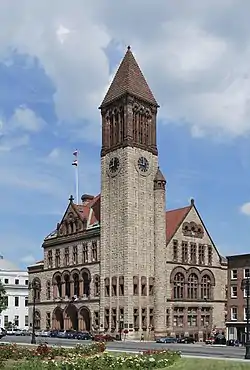 A brown and tan brick building with dark brown trim. The building has a tall bell tower on the nearest corner.