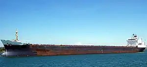 A rusty blue ship with a white superstructure with a clear blue sky
