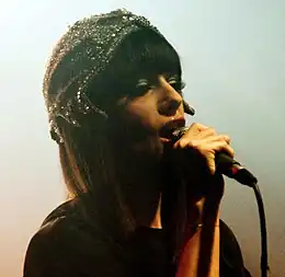  A white woman dressed in brown and a glowing hat performing a song.