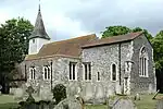 A flint church with a red tied roof and a tower at the west end, seen from the southeast