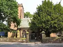 Photograph of the church from the south, showing the tower and part of the south aisle, partly obstructed by trees