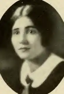 A yearbook photograph of a young white woman with dark hair parted center, wearing a dark garment with a round white collar