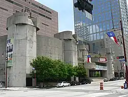 Concrete building in two sections, each with a five-sided tower on the ends. One is a curved and windowless. The other looks like a theater entrance with  rounded  marquee shapes and glassed entrance.