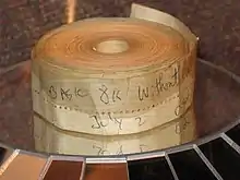 An aged roll of paper tape perhaps 1–2 inches (2.5–5.1 cm) wide; on the outside is written "BASIC 8K without cassette" and "July 2" in blue biro pen.