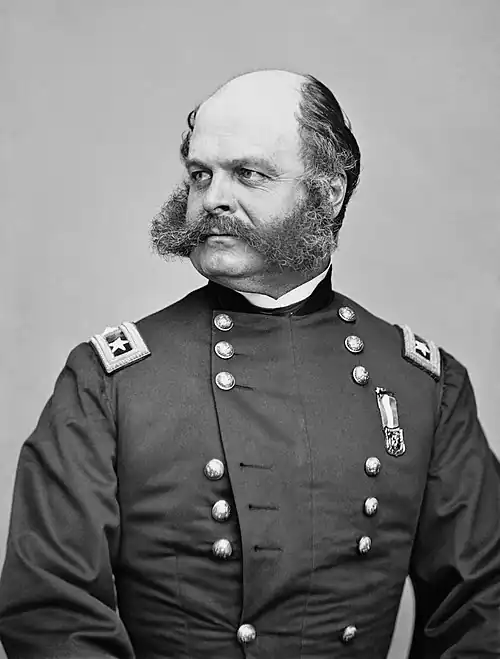 Black and white photo shows a man with an unusual moustache (but no beard) which joins very bushy sideburns. He wears a dark military uniform with the shoulder tabs of a U. S. major general.