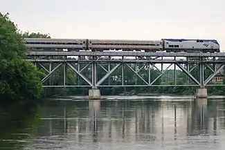 A passenger train crossing a truss bridge over a river