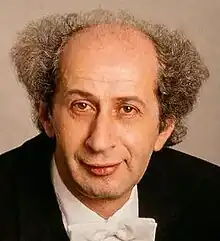 Man in his fifties in a formal suit, with curly, greying hair