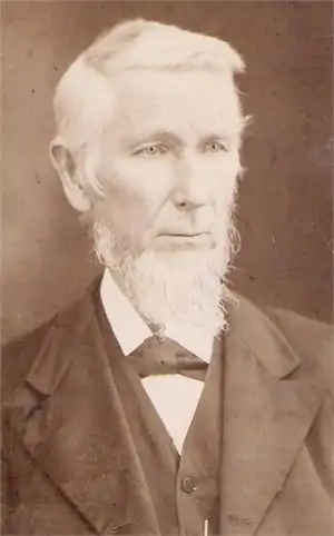 A sepia photo of a formally dressed, white-haired man