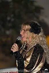 A picture of Andreea Bănică holding a microphone in her hand, wearing a black top.