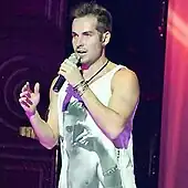 A man is seen performing while wearing a white crop top.