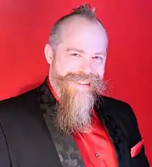 middle-aged Caucasian male in formal wear, with short hair and styled mustache and beard