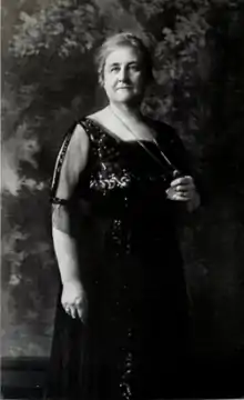 A middle-aged white woman, standing, wearing a dark sequined gown
