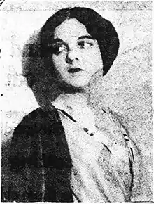 Grainy, black and white halftone photograph taken at bust length of woman looking off to the side