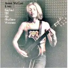 A three-quarter shot of the artist playing a six-string guitar. Her eyes are closed, she wears dark blue jeans and a t-shirt with the lettering Route 66 partly visible. She has short blonde hair and is facing forwards. At the top left is the artist's name and the word live in black lettering with the rest of the title in white lettering below that.