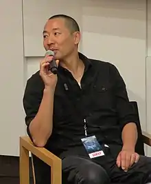 Ant Sang seated talking into a handheld microphone