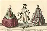 A fashion plate of three individuals, two white women modeling the casaquin: one green casaquin over a maroon dress with a wide crinoline and the second a maroon and green striped one over a matching dress. The casaquin is a coat that falls somewhere between the hips and knees and is wide enough around the skirt of the coat to lay over a wide-hooped skirt. The sleeves of these particular examples are wide and three-fourths length. It's fitted around the bodice.  There is a white man in the middle with a tricorn hat, an ivory jacket that reaches his knees with a flared skirt. It has loose sleeves with wide cuffs, and the coat is worn over white stockings and black boots. He has a walking stick in his hand.