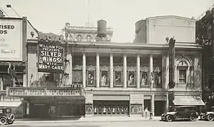 Theater building facade with colonnade spanning second and third stories and marquee and entrance on the left for two theaters.