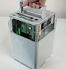 G4 Cube flipped upside down; a hand is pulling upward on a small handle, revealing green circuit boards and computer components within.