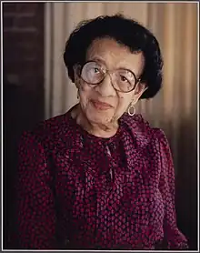 Photo portrait African American woman wearing pink ruffled blouse and glasses with short cropped black hair.