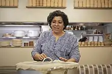 Woman standing behind a very large pot, the lid of which has been sealed with dough