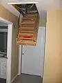 A retractable attic ladder halfway open.