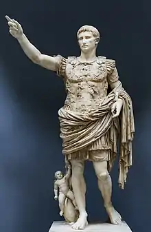 Photograph of a white marble statue of a man in Roman military dress, his right arm raised.