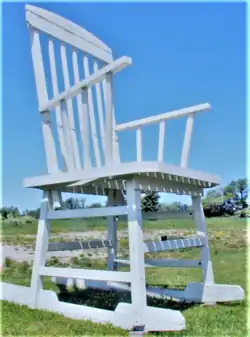 A large wooden rocking chair painted white against a blue sky and grass