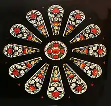 a small round stained glass window surrounded by twelve panels featuring floral designs of large red and small white flowers
