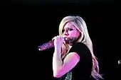 Avril Lavigne wearing a black gown and sining in to a microphone.