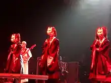 Yuimetal, Su-metal, and Moametal in black kimonos with their faces covered by a fox mask performing onstage
