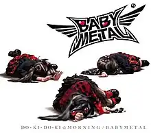 A white background with three girls in red and black clothes lying on the floor, the Babymetal logo on the top right, and the words "DO・KI・DO・KI ☆ MORNING / BABYMETAL" in black text along the bottom.