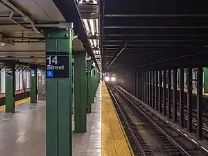 A view from the southbound platform of the BMT Broadway Line's 14th Street station. A "Q" train is arriving.