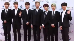 Group photo of BTS standing together wearing black suits with white shirts.