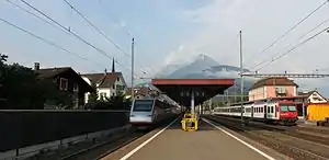 Island platform with passing trains and a station building to the right