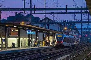 White train on tracks next to side platform in low light