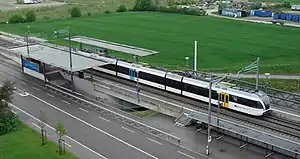 White train with black stripe pulling out of a station with two side platforms