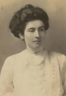 A young white woman with dark hair in a bouffant updo, wearing a high-collared white lacy blouse