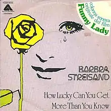 The vinyl sleeve of the record appears displaying a face with a tear drop falling from one eye behind a yellow rose atop a purple background.