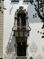 A wrought iron balcony which has a protruding and rounded base that tapers into a vertical section near the railing