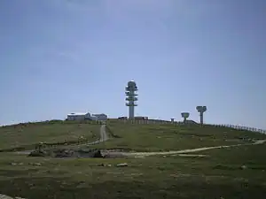 Three radio towers and several buildings on top of a mountain