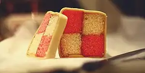 Homemade Battenberg cake covered in marzipan and, when cut in cross-section, displaying a distinctive two-by-two check pattern alternately coloured pink and yellow.