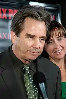 Aging Caucasian male with dark hair that is graying slightly.  He is wearing a black button-down shirt and green tie.
