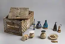 Painted wooden box with lid askew and its contents of stone and glass vessels neatly arranged beside it