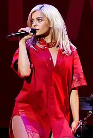 A young woman with long blonde hair, wearing a red dress, singing into a microphone